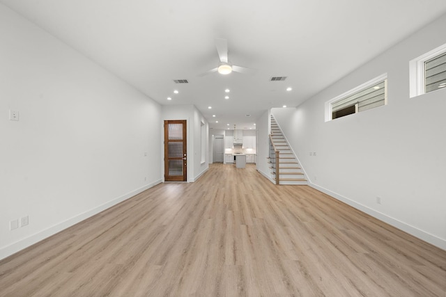 unfurnished living room featuring light wood finished floors, stairway, visible vents, and baseboards