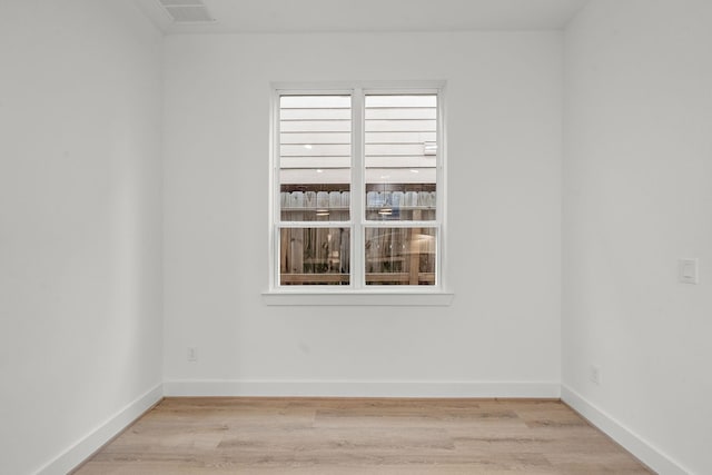 spare room featuring light wood finished floors, visible vents, and baseboards