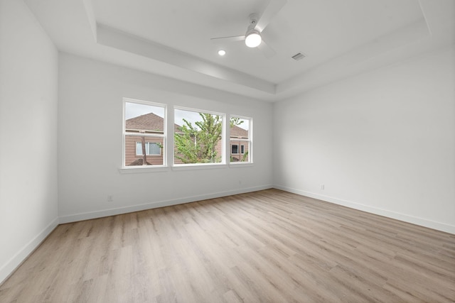 empty room with a tray ceiling, recessed lighting, ceiling fan, light wood-type flooring, and baseboards