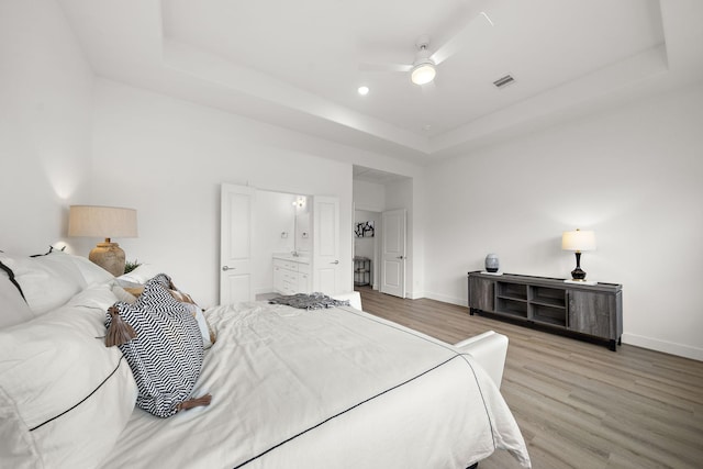 bedroom featuring wood finished floors, a raised ceiling, visible vents, and baseboards