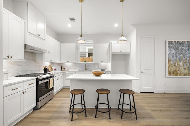 kitchen featuring stainless steel gas range, under cabinet range hood, pendant lighting, and light countertops