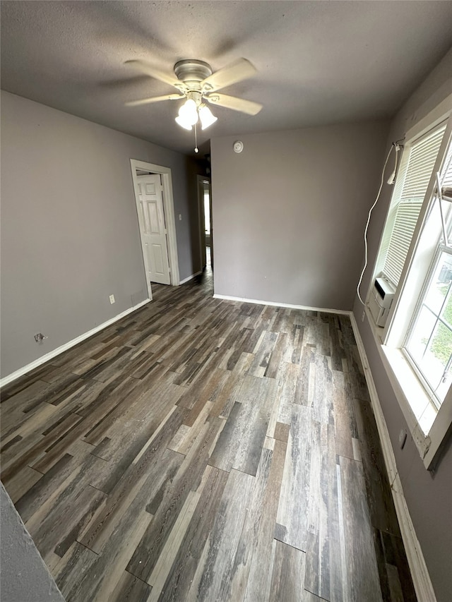 empty room featuring a ceiling fan, a healthy amount of sunlight, dark wood finished floors, and a textured ceiling