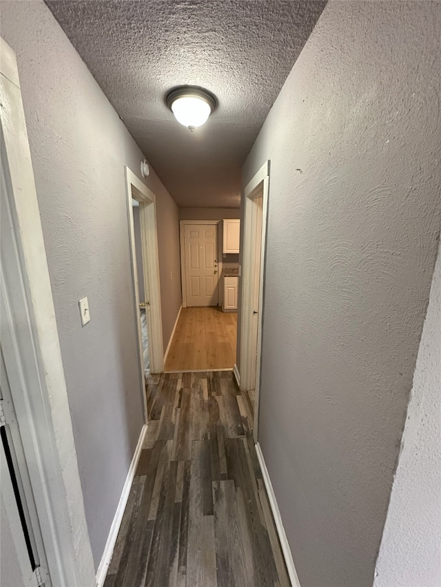 hallway featuring dark wood-style floors, baseboards, a textured ceiling, and a textured wall