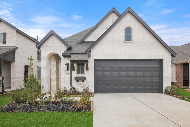 french provincial home with driveway, roof with shingles, a garage, and brick siding