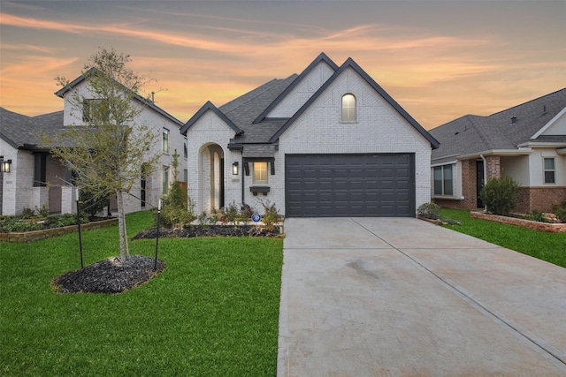 french country style house with concrete driveway, brick siding, a front lawn, and a shingled roof