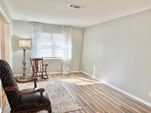 sitting room with a textured ceiling, wood finished floors, visible vents, and baseboards