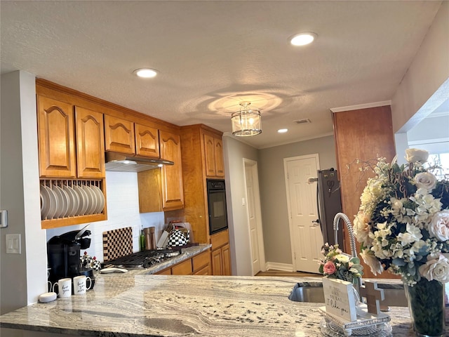 kitchen with a peninsula, under cabinet range hood, brown cabinets, and stainless steel appliances