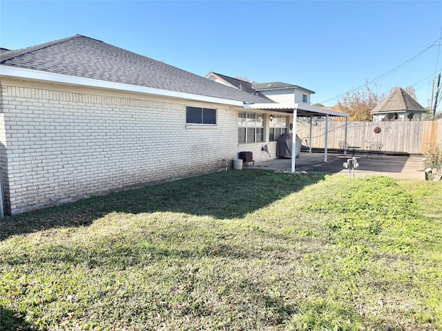 back of property featuring brick siding, a yard, a patio, a shingled roof, and fence