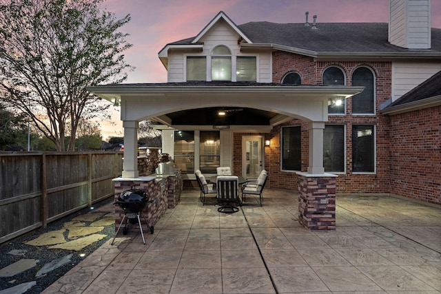 patio terrace at dusk featuring fence and a grill