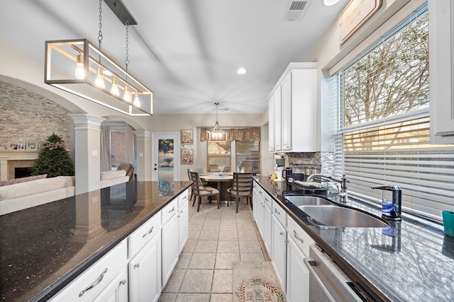 kitchen featuring arched walkways, decorative columns, hanging light fixtures, white cabinets, and a sink