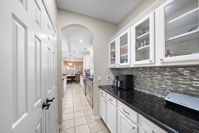 kitchen with light tile patterned floors, tasteful backsplash, arched walkways, glass insert cabinets, and white cabinetry