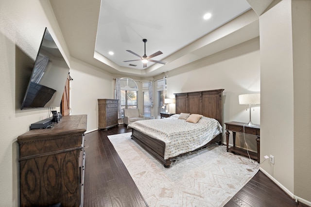 bedroom with arched walkways, a tray ceiling, dark wood-style flooring, and baseboards