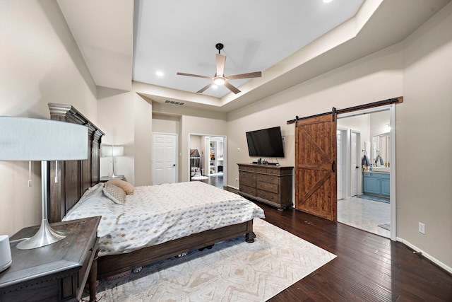 bedroom with a barn door, baseboards, visible vents, dark wood-type flooring, and a tray ceiling