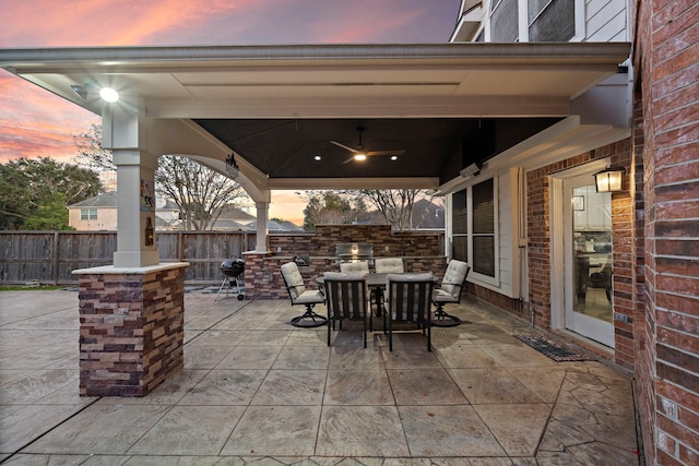 view of patio with a ceiling fan, area for grilling, fence, exterior kitchen, and outdoor dining space