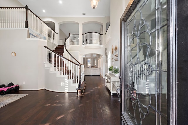 entryway with a towering ceiling, baseboards, stairway, and dark wood-style flooring