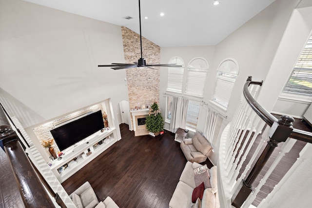 living area with a fireplace, visible vents, ceiling fan, wood finished floors, and high vaulted ceiling