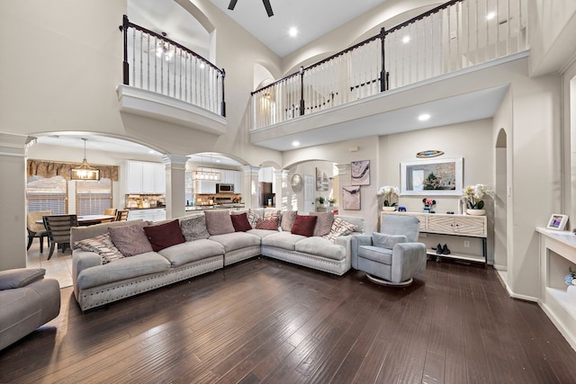 living room with arched walkways, dark wood-style flooring, a ceiling fan, and ornate columns