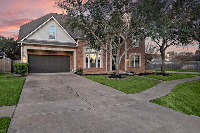 traditional-style house with driveway, roof with shingles, fence, a yard, and brick siding