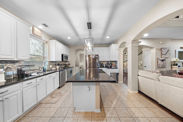 kitchen featuring arched walkways, stainless steel appliances, open floor plan, a center island, and dark countertops