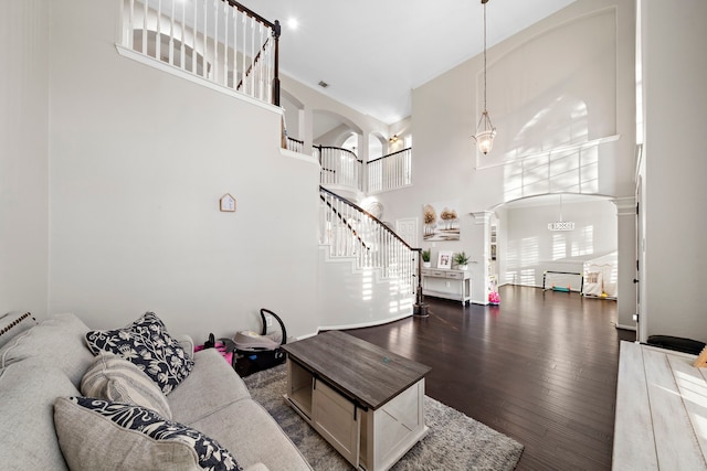 living area featuring decorative columns, arched walkways, a towering ceiling, stairway, and dark wood-style flooring