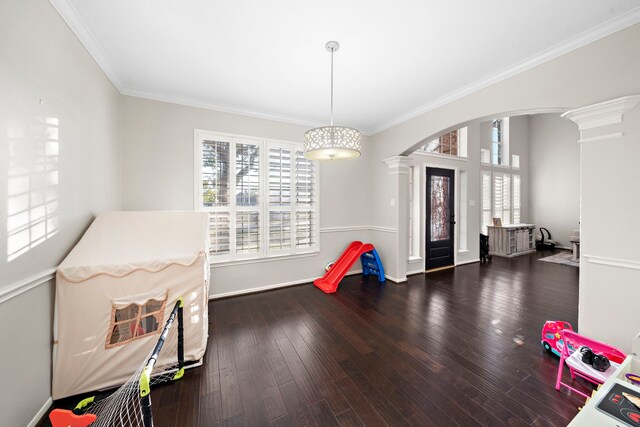 recreation room with arched walkways, dark wood-style flooring, baseboards, ornate columns, and crown molding