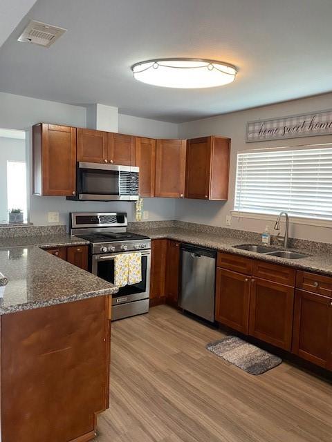 kitchen featuring visible vents, dark stone counters, appliances with stainless steel finishes, light wood-style floors, and a sink