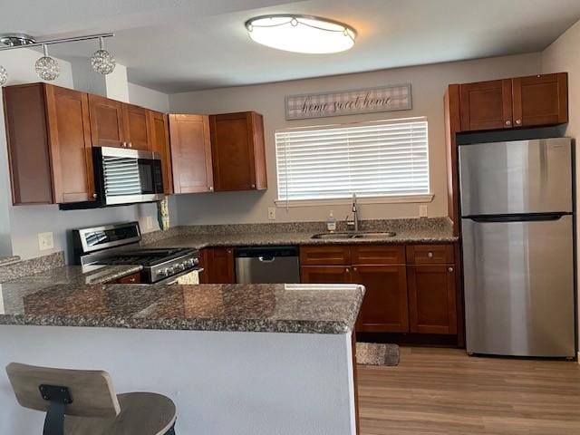 kitchen featuring a breakfast bar, stainless steel appliances, brown cabinetry, a sink, and a peninsula