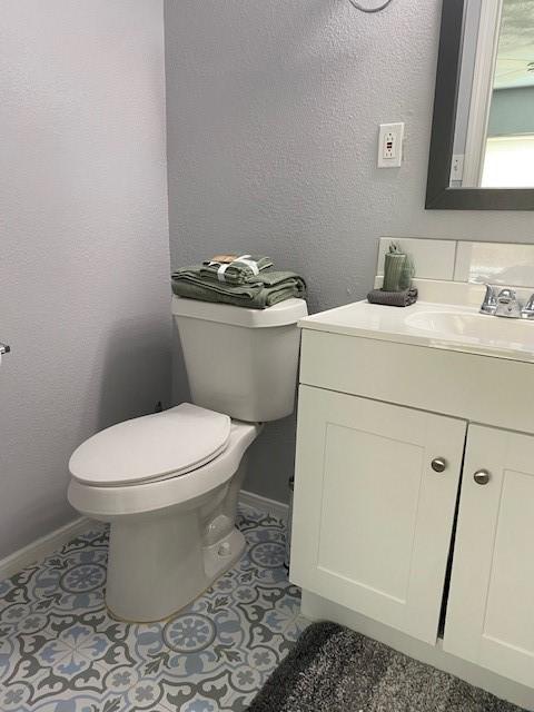 bathroom featuring baseboards, a textured wall, toilet, tile patterned floors, and vanity