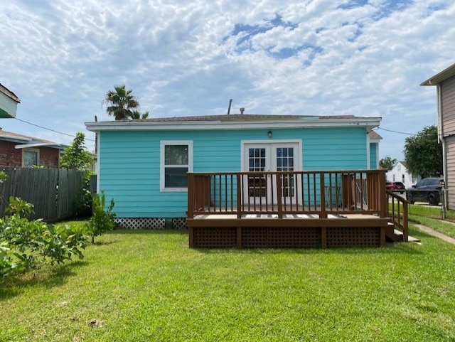 rear view of house featuring a lawn, a wooden deck, and fence