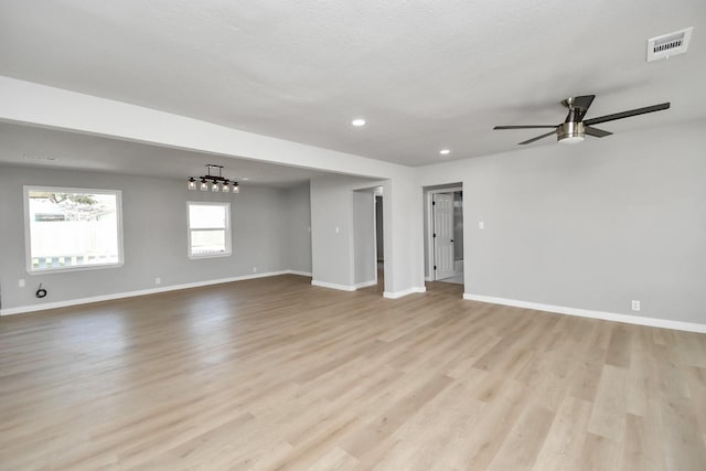 unfurnished room featuring visible vents, ceiling fan with notable chandelier, light wood-style flooring, and baseboards