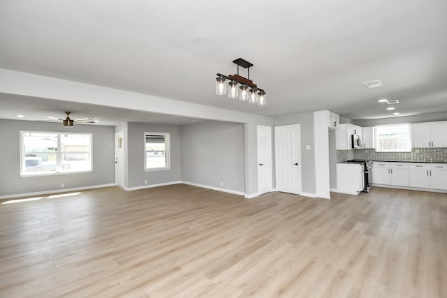 unfurnished living room featuring plenty of natural light, light wood-type flooring, visible vents, and baseboards