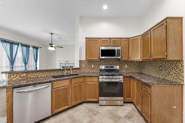 kitchen featuring stainless steel appliances, brown cabinetry, a sink, and a peninsula