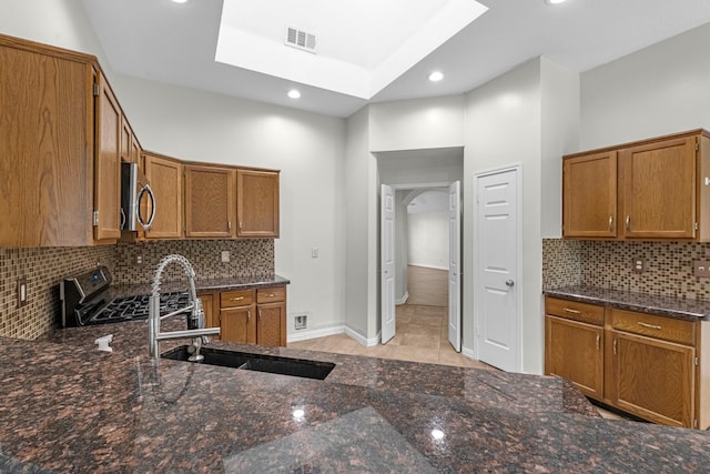 kitchen with brown cabinetry, stainless steel microwave, a sink, and gas range