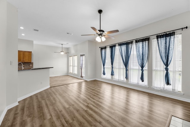 unfurnished living room with recessed lighting, baseboards, a sink, and light wood finished floors