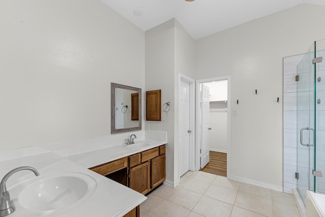 full bath featuring a walk in closet, double vanity, a stall shower, a sink, and tile patterned flooring