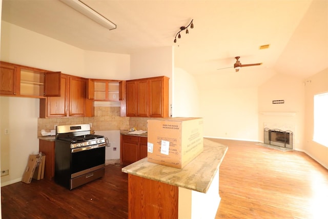 kitchen featuring brown cabinets, backsplash, a fireplace with flush hearth, open floor plan, and stainless steel gas range oven