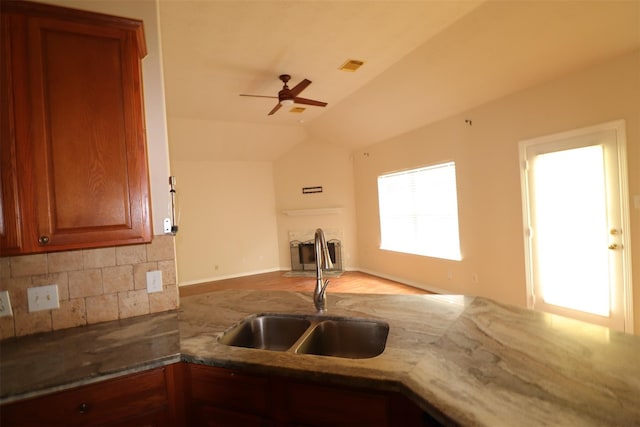 kitchen with lofted ceiling, stone countertops, a sink, open floor plan, and brown cabinets