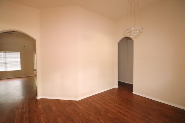 spare room with arched walkways, wood finished floors, and baseboards