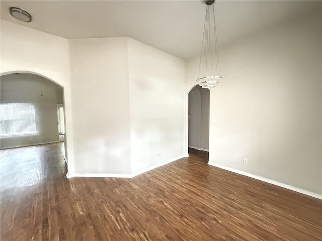 spare room featuring baseboards, arched walkways, and wood finished floors