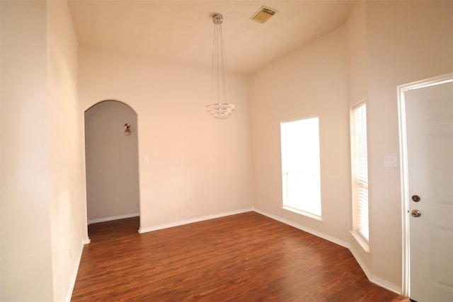 empty room with dark wood-type flooring, arched walkways, visible vents, and baseboards