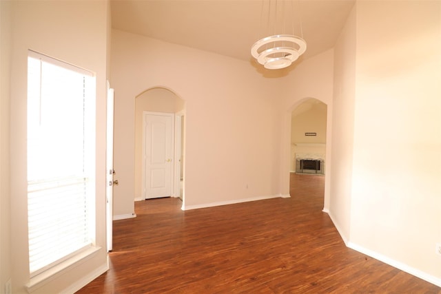 interior space featuring arched walkways, dark wood-style flooring, a fireplace, and baseboards