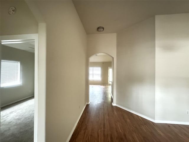 corridor featuring arched walkways, baseboards, and wood finished floors