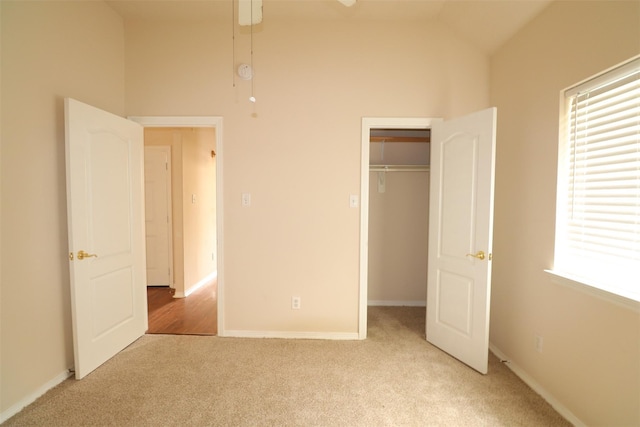 unfurnished bedroom with baseboards, light colored carpet, lofted ceiling, a spacious closet, and a closet