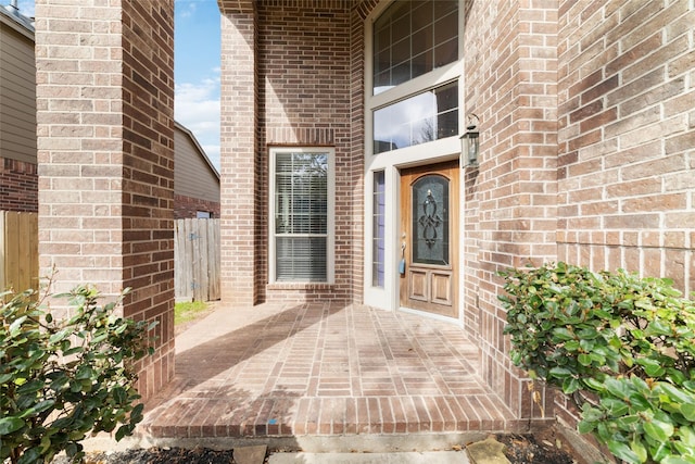 doorway to property featuring fence, a patio, and brick siding