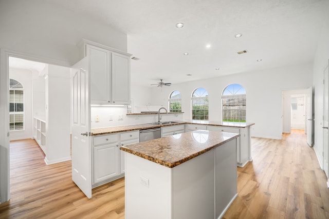 kitchen featuring a peninsula, a sink, a kitchen island, white cabinetry, and dishwasher