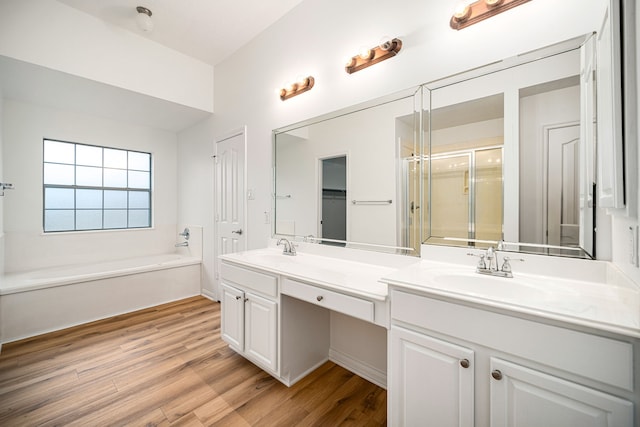 full bath with double vanity, a sink, a bath, and wood finished floors