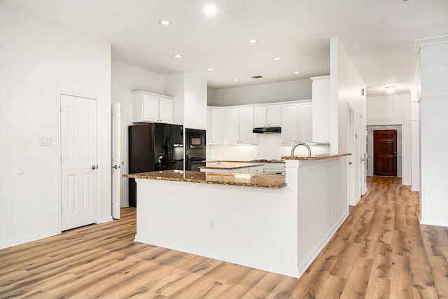 kitchen with white cabinets, a peninsula, under cabinet range hood, stone counters, and black appliances