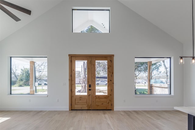 foyer with light wood finished floors, a healthy amount of sunlight, high vaulted ceiling, and baseboards