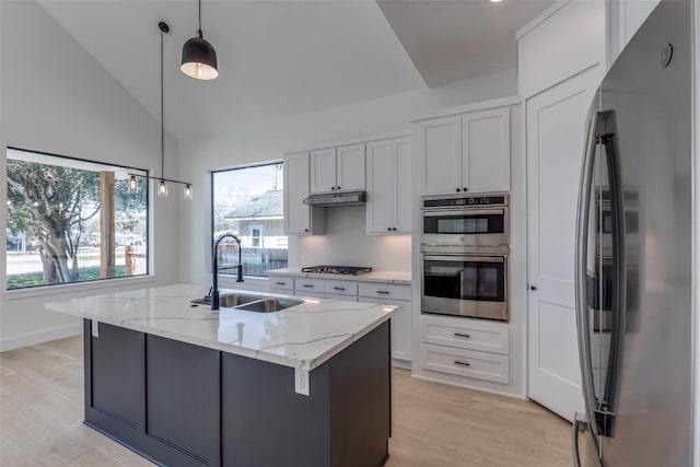 kitchen featuring under cabinet range hood, decorative light fixtures, light stone counters, appliances with stainless steel finishes, and a sink