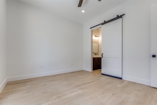 unfurnished bedroom with connected bathroom, a barn door, baseboards, and light wood-style flooring